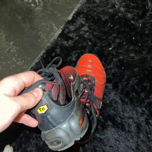 Nike Air Max Plus Tn röd/svart 43 - Nike Air Max Plus Tn sneakers i rött och svart med coola vågformade detaljer och synlig Air Max-dämpning i sulan. Skorna har snörning, mesh och syntetmaterial, samt Tn-logga på häl och sula. Perfekt för dig som gillar streetwear och sportig stil.