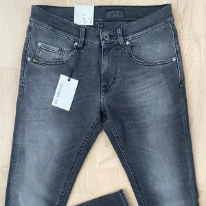 Grå skinny jeans Tiger of Sweden - Helt nya grå jeans från Tiger of Sweden med slim fit passform. Jeansen har en riktigt snygg slitning vid benet samt bakfickorna och tydliga sömmar. Tillverkade i stretchig denim från italien för en bekväm passform. Perfekta för dig som gillar en modern och stilren look med många små detaljer.