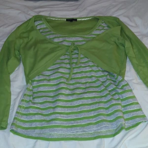 Grön randig kofta från Cpm - Snygg grön kofta från Cpm med knyt framtill. Under finns en grå och grön randig topp i mjuk bomull. Långärmad och perfekt för lager-på-lager-look. Passar dig som gillar färg och vill sticka ut lite extra.