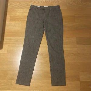 Slim rutig kostymbyxa Jack & Jones - Slim fit kostymbyxa från Jack & Jones i grått med snyggt rutigt mönster. Klassisk design med bälteshällor, framfickor och bakfickor med knapp. Perfekt för dig som gillar stilrena och moderna byxor med lite edge.