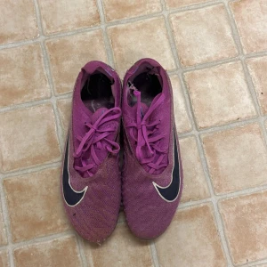 Nike Phantom GX Elite SE FG Thunder Pack  - Säljer ett par lila Nike fotbollsskor med snörning, är i ett helt okej skick men allt annat är mycket fint. Nypriset är 3200 och eftersom de har tagit några smällar så säljer jag dem för 1200! Storlek är 37,5
