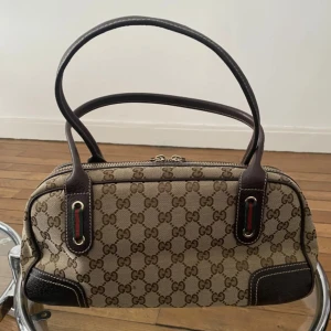 Gucci handväska med GG-mönster - Snygg handväska från Gucci med klassiskt GG-mönster i beige och brunt. Väskan har mörkbruna skinn-detaljer, dubbla handtag och dragkedja upptill. Insidan är märkt med 'Gucci made in Italy'. Köpt från Vestaire collective, vill man ha mer bilder så hör av dig!