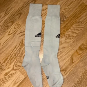 Adidas fotbollsstrumpor - Säljer ett par vita fotbollsstrumpor från Adidas med svart logga. Perfekta för fotboll eller träning, med ribbade muddar upptill för extra komfort. Storlek 3.