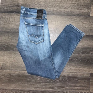 Replay Anbass hyperflex jeans  - Snygga Replay Hyperflex Anbass jeans i blå tvätt med coola slitningar och klassiska fem fickor. Stretchigt material som sitter skönt. Midja 42cm, längd 101cm. Storlekslappen med L storleken  är borta men jag bedömer den till L32 men utgå ifrån måtten :) JAG SKICKAR EJ FLER BILDER NÄR JAG BÄR JEANSEN! för storleksguide hänvisar jag till måtten och för bättre inblick i passformen rekommenderar jag att googla på modellnamnet :) s3