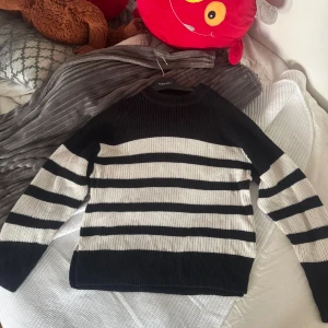 Randig stickad tröja från Gina Tricot - Säljer en svart och vit randig stickad tröja från Gina Tricot i storlek 158/164. Tröjan har en klassisk rund halsringning och långa ärmar. Perfekt för dig som gillar en enkel men snygg stil med tydliga kontraster.