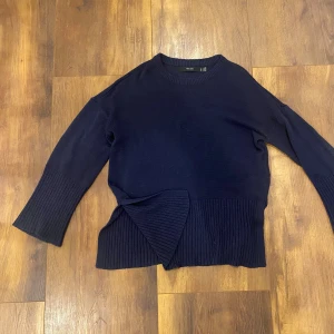 Mörkblå stickad tröja med omlott - Säljer en mörkblå stickad tröja från Vero Moda med bred ribbad mudd och snygg omlottdetalj i nederkant. Tröjan har långärmade ärmar och en klassisk rund halsringning. Perfekt för dig som gillar stilrena och trendiga plagg.
