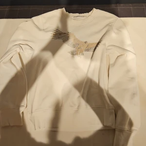 Vit sweatshirt med örn från J.Lindeberg - Vit sweatshirt från J.Lindeberg Denim med stor örn-tryck på bröstet. Tröjan har rund hals, ribbade muddar och är tillverkad i mjuk bomull. Perfekt för dig som gillar stilrena plagg med coolt motiv.