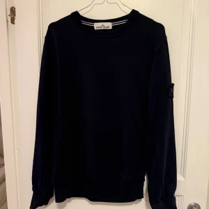 Svart sweatshirt från Stone Island - En stilren svart sweatshirt från Stone Island. Perfekt för dig som gillar enkel och snygg streetwear. Den har ett litet hål som syns på andra bilden men inget som syns så tydligt
