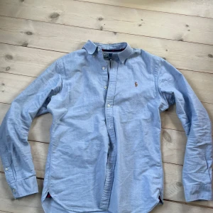 Blå skjorta Polo Ralph Lauren M - Snygg ljusblå skjorta från Polo Ralph Lauren i slim fit. Klassisk design med knappar hela vägen, button-down krage och broderad logga på bröstet. Skjortan är långärmad och tillverkad i mjuk bomull som känns skön mot huden. Kan gå ner i pris vid snabb affär! Skriv om du har någon fråga!