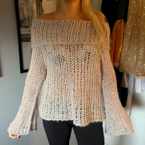 Beige offshoulder stickad tröja - Säljer en beige stickad tröja med bred offshoulder-ringning och långa ärmar. Tröjan har grovstickad struktur och är lite transparent, vilket ger en chill och trendig vibe. Perfekt för dig som gillar avslappnad och snygg stil.