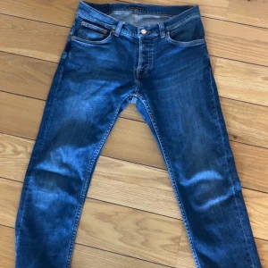 Nudie Jeans - Snygga blå jeans från Nudie Jeans med klassisk femficksdesign och kontrastsömmar på bakfickorna. Modellen är skinny med smal passform och har orange detaljer vid knappar och sömmar. Perfekt för dig som gillar stilrena och moderna jeans.