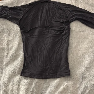 Svart långärmad topp från Gina Tricot - En svart, figurnära långärmad topp från Gina Tricot i storlek XS. Tillverkad i ett tunt och mjukt material som känns skönt mot huden. Perfekt att styla med jeans eller kjol för en clean look.