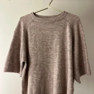 Beige stickad tröja från 157 - Mysig beige stickad tröja från 157 med rund halsringning och kortare ärmar. Tröjan har en avslappnad passform och är perfekt för lager-på-lager. Enkel och stilren design som funkar till många olika looks.
