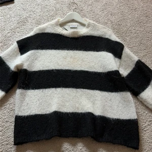 Randig stickad tröja från Noisy May - Mysig stickad tröja från Noisy May med breda svarta och vita ränder. Tröjan har en loose passform, rund halsringning och långa ärmar. Perfekt för lager-på-lager under kyliga dagar.