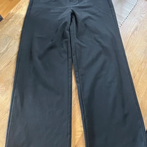 Svarta kostymbyxor från Object - Svarta kostymbyxor från Object med rak passform och resår i midjan baktill. Byxorna har hällor för bälte, snedställda fickor fram och fuskfickor bak. Perfekta för en clean och stilren look.