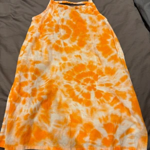 Orange tie-dye klänning från H&M - Superfin kort klänning från H&M i orange och vitt tie-dye mönster. Den har smala axelband och en avslappnad passform, perfekt för varma dagar. Materialet är lätt och luftigt, vilket gör den skön att bära under sommaren. 