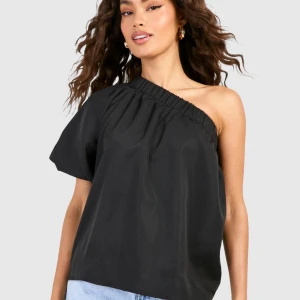 Svart oneshoulder topp med volym - Säljer en svart oneshoulder topp med lös passform och voluminös ärm på ena sidan.. Storlek 36. Aldrig använd