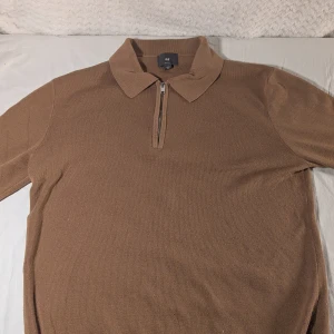 Brun stickad polotröja från H&M - Snygg brun stickad polotröja från H&M i slim fit-modell. Tröjan har klassisk krage och halv dragkedja framtill för en stilren look. Perfekt för lager-på-lager och passar till både jeans och chinos.