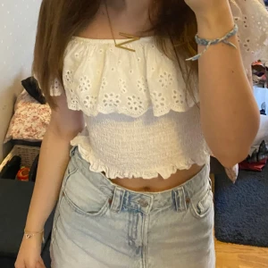Vit offshoulder croppad blus - Supersöt vit offshoulder blus i croppad modell med volang och broderade blommor upptill. Smockad överdel och volangkant nertill. Tillverkad i 100% viskos, perfekt för varma dagar och sommarvibba🤍Osäker på storlek, men passar mig som är XS/S. Stretchigt material så passar säkert M. 100% viscose 