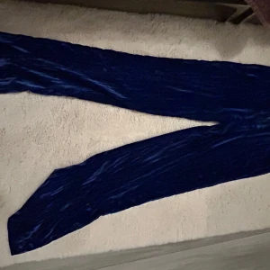 Blå sammetsbyxor från Lindex - Mörkblå sammetsbyxor från Lindex i storlek 36. Byxorna har en mjuk och glansig yta som ger en lyxig känsla. De har raka ben och en klassisk passform, perfekta för dig som vill sticka ut lite extra.