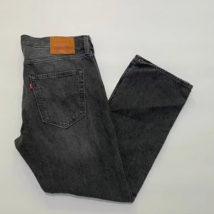 Levi's 501 svarta jeans W36 L30 - Klassiska svarta Levi's 501 jeans med rak passform och knappgylf. Jeansen har en snygg tvättad look, fem fickor och ikonisk läderpatch bak i midjan. Perfekta för dig som gillar en tidlös och avslappnad stil.