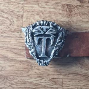 Vintage Tiger of Sweden bälte - Brunt läderbälte från Tiger of Sweden med ett unikt silverfärgat spänne, format som ett tigerhuvud. Vintage. Har för mig att denna inte säljs längre.  Storlek 85CM/31-35" Mycket bra skick (se bilder