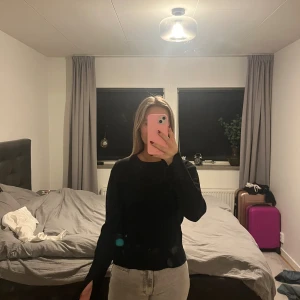 Svart stickad tröja med slits vid ärm - Svart stickad tröja med lång ärm och cool slitsdetalj vid ärmslutet. Tröjan har en klassisk rund halsringning och en något loose passform. Perfekt för dig som gillar stilrena plagg med en twist.