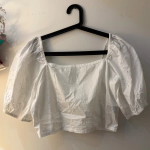 Vit blus med puffärm från H&M - Säljer en vit blus från H&M i storlek L med fyrkantig urringning och puffiga, broderade ärmar. Blusen har smockad rygg och elastiska ärmslut. Materialet är mjuk bomull och detaljerna på ärmarna ger en romantisk vibe. Perfekt för dig som gillar trendiga och söta toppar.