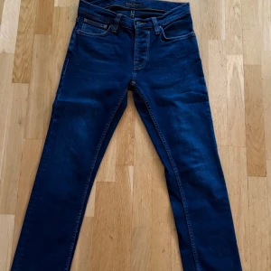 Mörkblå jeans från Nudie Jeans - Snygga mörkblå jeans från Nudie Jeans i klassisk femficksmodell. Jeansen har en rak passform med normal midja och är tillverkade i mjukt denimtyg. Perfekt för dig som gillar stilrena och tidlösa jeans med diskreta detaljer.