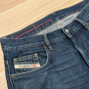 Blå jeans från Diesel Industry - Size 32/30. Säljer ett par klassiska blå jeans från Diesel Industry med raka ben och normal passform. Jeansen har snygga kontrastsömmar, fem fickor och en diskret logga på myntfickan. Perfekta för dig som gillar en tidlös och avslappnad look.