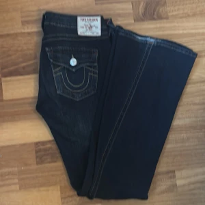 True Religion mörkblå bootcut jeans - Snygga mörkblå jeans från True Religion med klassiska kontrastsömmar och ikoniska fickdetaljer med silverknappar. Modellen har bootcut-ben och låg midja, tillverkade i slitstarkt jeansmaterial. Fick dom i födelsedagspresent men vart inte nöjd med färgen så därför säljer jag dem. Priset kan diskuteras vid snappt köp 