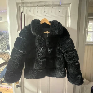 Svart pälsjacka med krage - Säljer en svart pälsjacka med fluffig struktur och bred krage. Jackan har en boxig passform och långa ärmar, perfekt för att hålla sig varm och snygg under vintern 🥰