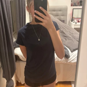 Mörkblå polotopp från 157 - Säljer en mörkblå polotopp från 157 i mjuk bomull. Toppen har korta ärmar och en högre hals, med snygg snörning på ena sidan för extra stil. Perfekt att matcha med jeans eller kjol för en clean look.