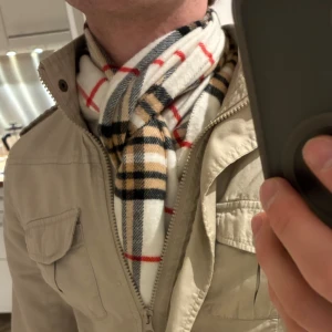 Rutig halsduk från Gerard Pasquier - Snygg halsduk med klassiskt rutigt mönster i vitt, beige, svart och röda linjer. Mjuk och skön, tillverkad av viskos och akryl. Perfekt längd för att vira runt halsen och har fransar i ändarna. Passar dig som gillar stilren och tidlös design.