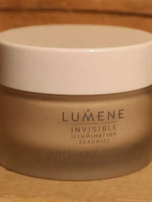 Lumene Instant Glow Skin Tint - Fräsch hudtonad gelkräm från Lumene i en rund burk med vit lock. Produkten heter Invisible Illumination Kaunis Instant Glow Fresh Skin Tint och ger en naturlig lyster. Färgen är ljusbeige och formulan är lätt och återfuktande.