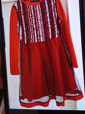 Röd paljettklänning med lång ärm - Säljer en röd klänning med lång ärm och glittriga paljetter på överdelen. Kjolen är i tunt, transparent tyg med ett rött underlager. Klänningen har rund hals och är knälång, perfekt för dig som gillar att sticka ut med lite extra glitter.