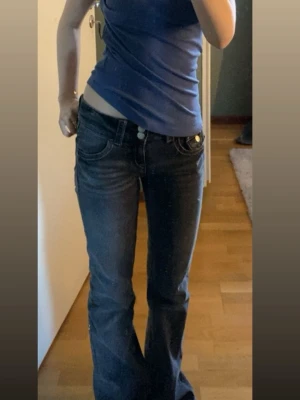 Grå bootcut jeans från Gina Tricot - Säljer ett par grå jeans från Gina Tricot i storlek 152. Modellen är bootcut med låg midja och har snygga detaljer som markerade sömmar och fickor med knapp bak. Jeansen är tillverkade i klassiskt denimtyg och har en cool tvättad look.