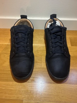 Mörkblåa Louboutin sneakers - Säljer ett par svarta sneakers från Christian Louboutin i storlek 45. Skorna har klassisk röd sula, svart ovandel i textil och skinn, samt broderad Louboutin-logga på hälen. Insidan är fodrad i beige skinn för extra komfort. Pris kan såklart diskuteras! 🤝