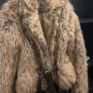 Beige pälsjacka med bälte - Säljer en supercool beige pälsjacka med bälte. Den är perfekt för att hålla sig varm och snygg under kyliga dagar. Jackan har en fluffig look och är i mycket bra skick. Perfekt för höst och vinter!