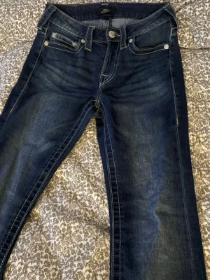 True Religion BECCA Bootcut Jeans Midwaist - Säljer ett par mörkblå True Religion BECCA jeans med bootcut och snygga kontrastsömmar. Klassiska broderade bakfickor och midwaist passform. Så snygga men passar mig inte längre. Använt 2 gånger. Är ungefär 160 och är lite långa.