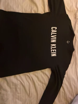 Svart långärmad tröja Calvin Klein - Säljer en svart långärmad tröja från Calvin Klein med stor vit logga över bröstet. Tröjan har en klassisk passform. Supermjukt material!