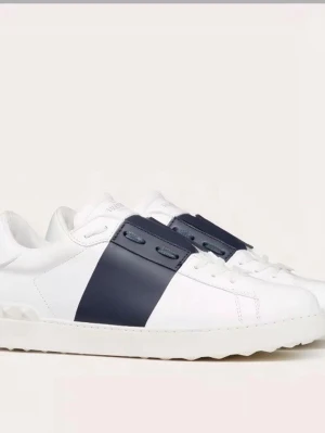 Valentino Garavani Open sneakers - Snygga vita sneakers från Valentino Garavani med bred marinblå rand över mitten. Skorna har snörning, rund tå och platt sula med ikoniska nitar på hälen. Tillverkade i skinn för en lyxig känsla och stilren look. Perfekta för dig som gillar exklusiva detaljer.