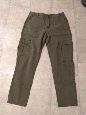Olivgröna cargobyxor från Cubus - Säljer ett par olivgröna cargobyxor från Cubus med klassiska sidofickor och rak passform. Byxorna har knapp och dragkedja i midjan samt är tillverkade i mjuk bomull. Perfekta för en avslappnad och cool stil.