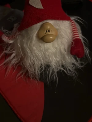 Julig tomteväst med röd-vit design - En rolig och mysig tomteväst med lång, vit, fluffig fuskpäls och röda detaljer. Västen har en röd luva med hjärtdetalj och randiga röda och vita ärmar. Perfekt för att maxa julkänslan och sticka ut på julfirandet.