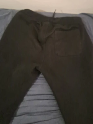 Svarta mjukisbyxor från Sail Racing - Svarta mjukisbyxor från Sail Racing med vit logga längs benet och snörning i midjan. Byxorna har en bakficka och en vit rand längs midjan. Perfekta för chill eller träning, tillverkade i mjukt material.