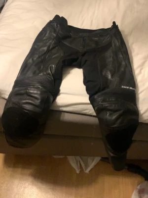BMW Motorrad motorcykel skinnbyxor - Säljer ett par svarta skinnbyxor från BMW Motorrad, perfekta för dig som kör hoj. Byxorna har förstärkta partier vid knäna. OBS dragkedjan som håller ihop jacka me byxor är sönder. (Se bild 3). Krachpuckar har jag inte på men kan köpas och sättas på