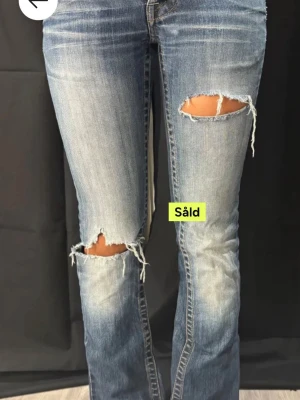 Blå slitna bootcut jeans Koola Anna - Snygga blå jeans från Koola Anna med bootcut-modell och slitna detaljer vid knäna. Jeansen har en klassisk femficksdesign, normal passform och är tillverkade i jeansmaterial. Perfekta för dig som gillar en avslappnad och trendig look.