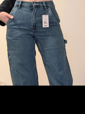 Blå wide jeans Labor XS - Säljer ett par blå jeans från Labor i storlek XS. De har hög midja, breda ben och klassiska fickor fram och bak. Jeansen är tillverkade i bomull och har en cool, loose passform med en extra detalj på sidan av benet.