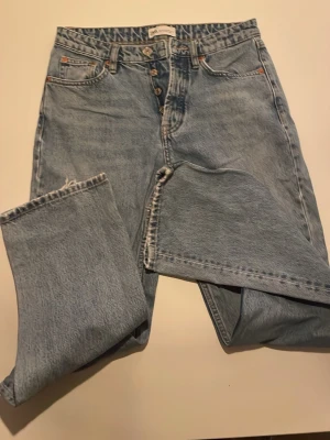 Ljusblå raka jeans från Zara - Säljer ett par ljusblå jeans från Zara med raka ben och hög midja. Klassisk femficksmodell med knappgylf och snygga detaljer i metall. Jeansen är i ett mjukt bomullsmaterial och har en avslappnad passform. Ena fickan bak saknas.