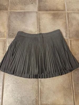 Grå plisserad kortkjol från H&M - Hej!👋Jag säljer en snygg grå plisserad kortkjol från H&M i storlek 44, jag skulle säga att passformen är lite mindre📏Kjolen har bred linning och klassiska veck som ger ett stilrent intryck. Materialet består av 70% polyester och 30% viskos vilket gör den både mjuk och lätt att bära.🙌 Skriv gärna om du har frågor💞